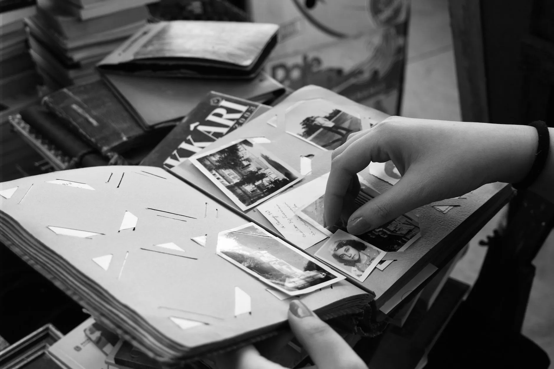 A hand lifting loose photographs from the black paper pages of an old magnetic photo album