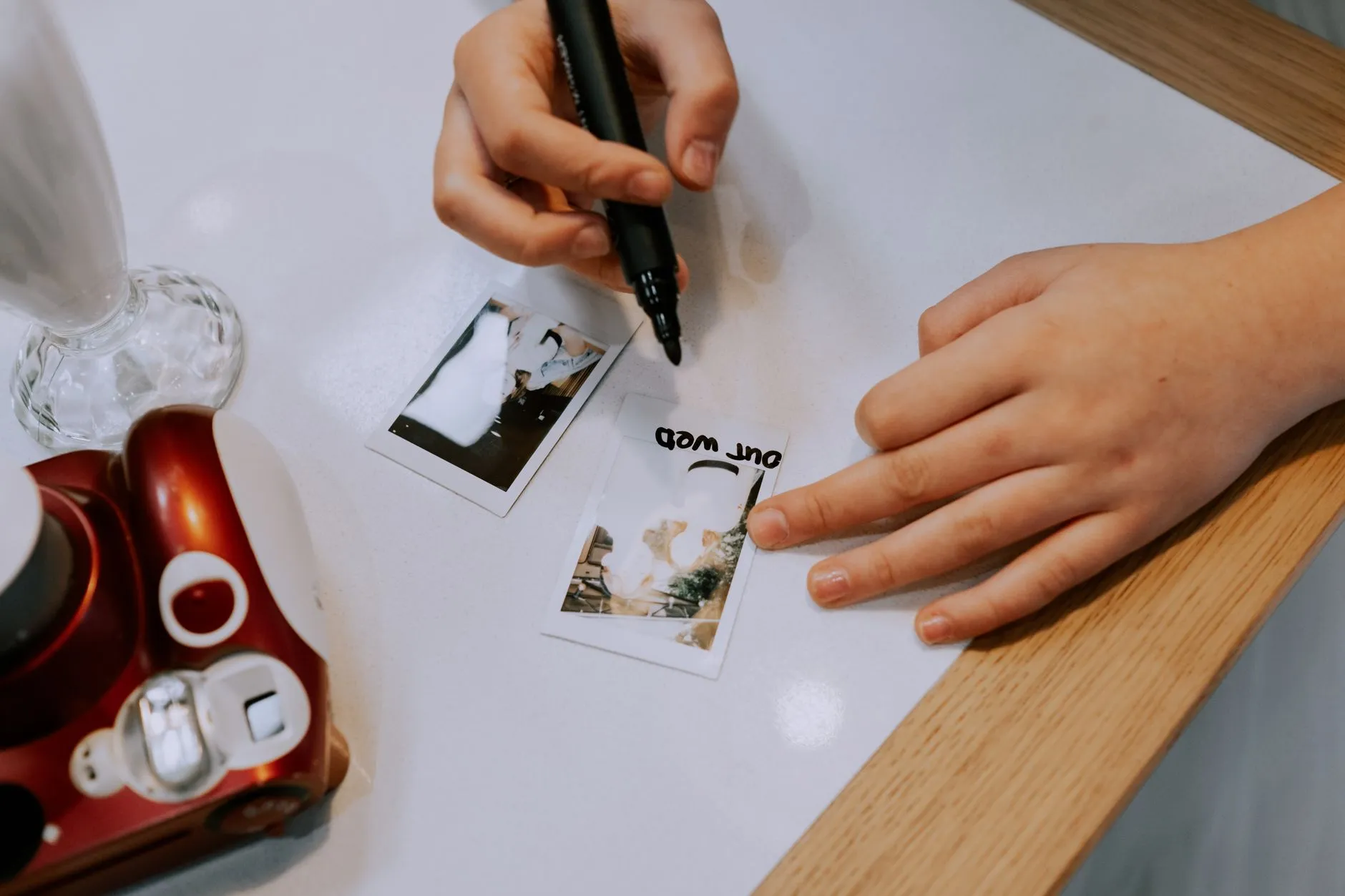 A hand holding a marker pen and writing directly onto small instant photographs on a table