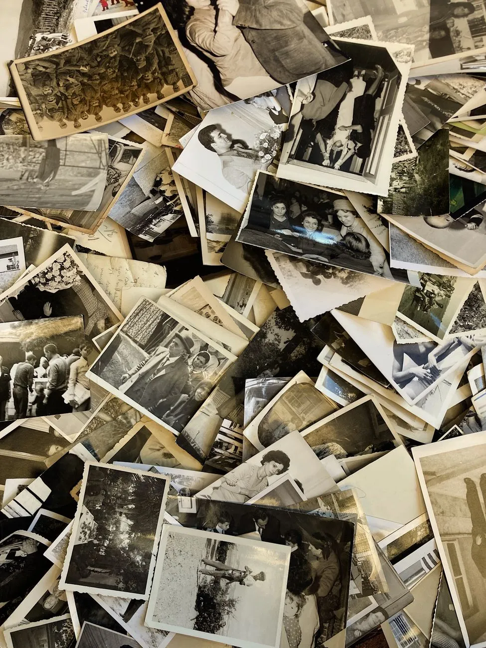 A sprawling, uncatalogued pile of hundreds of vintage black and white family photographs covering a table