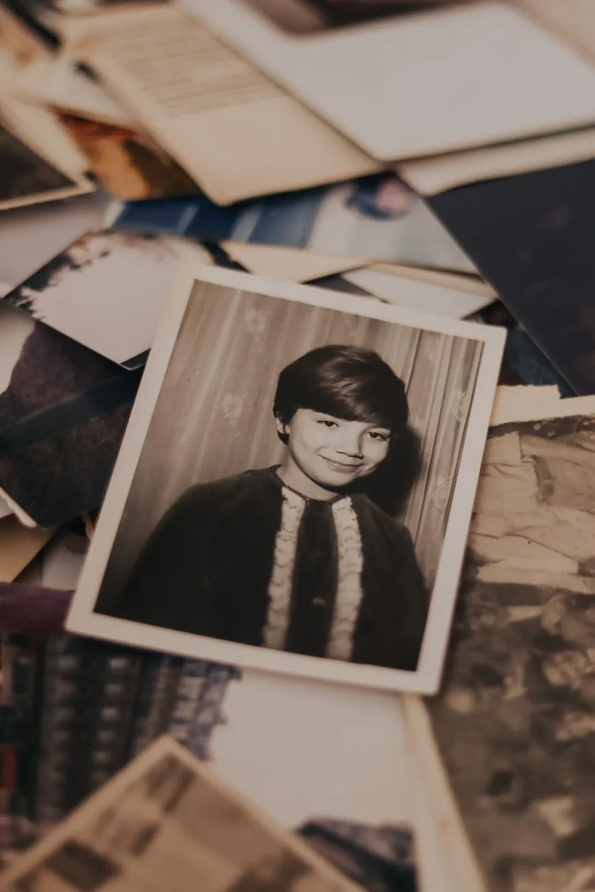 A vintage black and white portrait print resting on top of a jumbled pile of old family photographs and envelopes